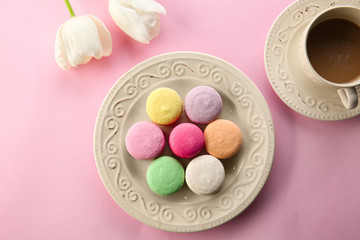 Plate with tasty macarons, cup of coffee and flowers on color background, top view