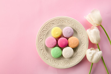Plate with tasty macarons and flowers on color background, top view