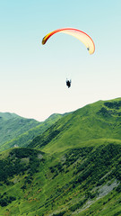 A paraglider with people flies over the mountain peaks in a bright blue sky.