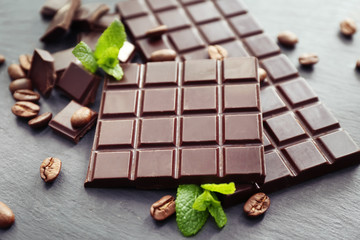Tasty dark chocolate and coffee beans on table, closeup