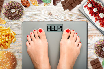 Diet temptation or hard to lose weight concept with woman weighing on bathroom scale with many...