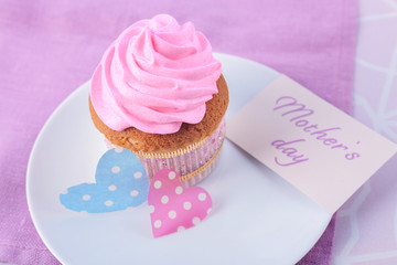Tasty cupcake and card with words MOTHER'S DAY on color background