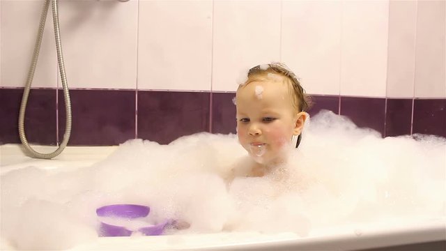 little happy girl bathes in the bathroom with foam. He plays with foam.