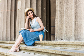 young smiling woman with tablet and coffee to go sitting on steps