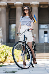 Fototapeta na wymiar stylish young woman in sunglasses with retro bicycle standing on street