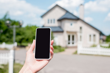 Cropped image of young woman holding smartphone with blank screen in front of house