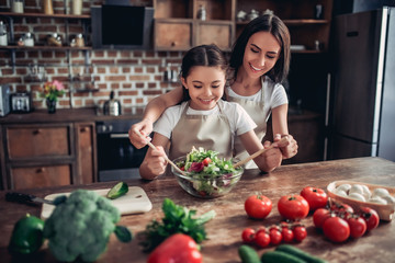 mother helping her daughter tossing the salad