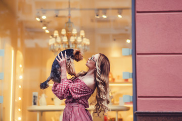 Stylish woman kissing little dog in city.