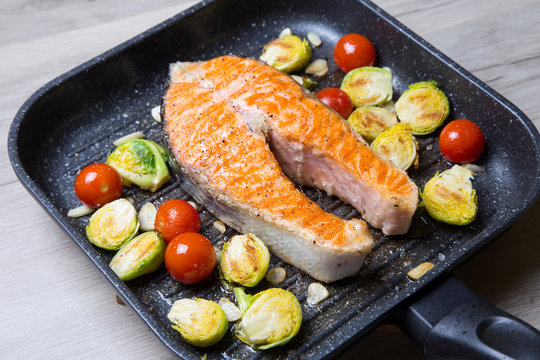 Salmon steak with Brussels sprouts, cherry and garlic in a pan grill. Close-up, selective focus.