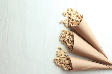 Paper cones with tasty cashew nuts on white wooden background