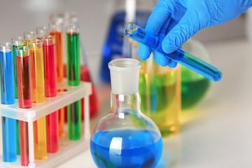 Laboratory worker pouring liquid from test tube into flask at table, closeup