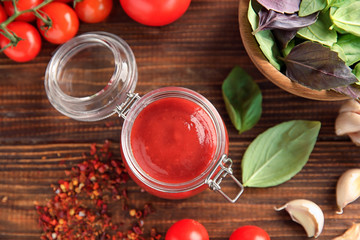 Delicious red sauce in glass jar and ingredients on table, top view