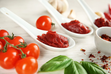 Delicious red sauce in ceramic spoons and ingredients on table