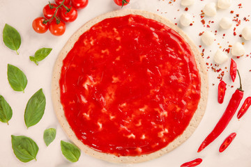 Raw dough for pizza with red sauce and ingredients on light background, top view