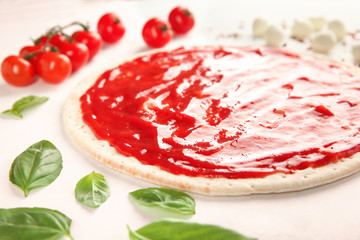 Raw dough for pizza with red sauce and ingredients on table