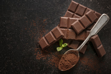 Spoon with cocoa powder and tasty chocolate on dark background, top view