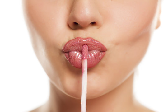 Fototapeta young beautiful woman apply a lip gloss on her lips on white background