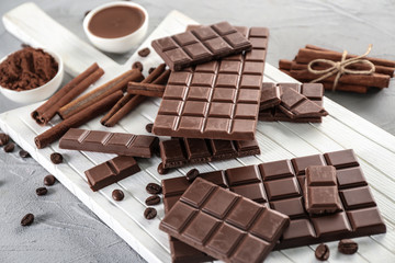 Composition with tasty chocolate, coffee beans and cinnamon sticks on wooden board