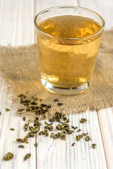 Cup with green tea, tea leaf and lemon on linen burlap on white wooden background