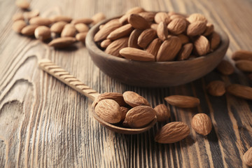 Bowl and spoon with almonds on wooden background