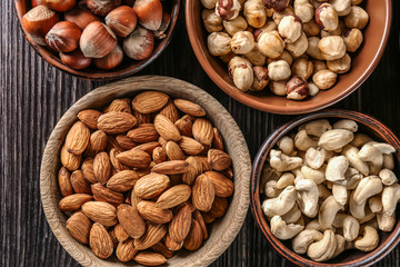 Bowls with different nuts on wooden table, top view