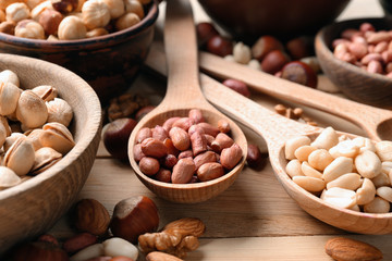 Bowls and spoons with different nuts on wooden table, closeup
