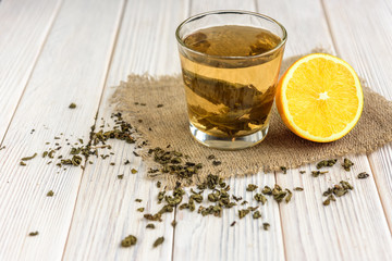 Cup with green tea, tea leaf and lemon on linen burlap on white wooden background