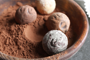 Fototapeta na wymiar Chocolate candies in bowl with cocoa powder, closeup