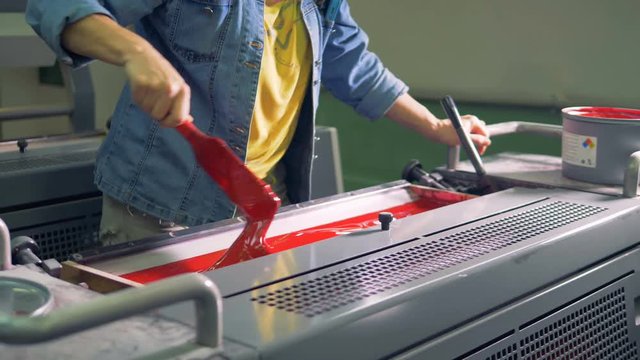 A man takes paint from a can and puts it into printing machine.