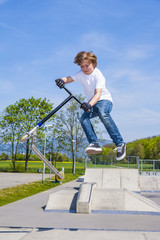 boy has fun jumping with the push scooter at the skate park