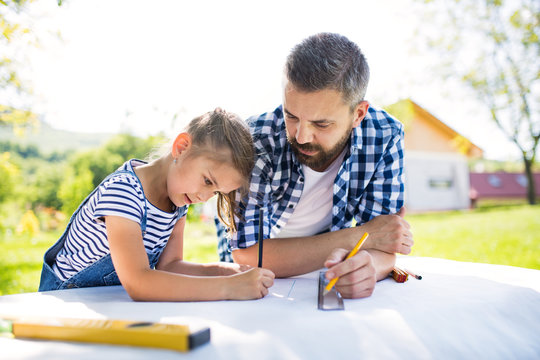 Father with a small daughter outside, planning wooden birdhouse.