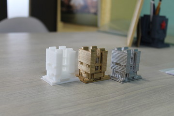 the model of the house is printed on a 3d printer. 3 models of white, gold and silver color standing next to each other.