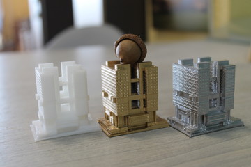 the model of the house is printed on a 3d printer. 3 models of white, gold and silver colors standing next to each other. on the roof of the Golden house is an acorn.