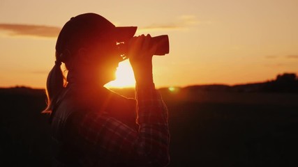 A woman looking through binoculars at sunset. Travel and safari concept - Powered by Adobe