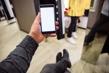 man looking into phone while his girlfriend do shopping in boutique