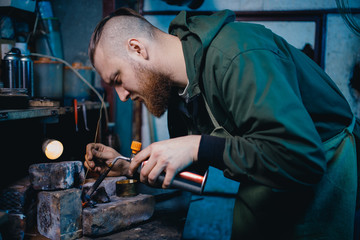 Smith jeweler produces silver metal smelting, holds gas burners in his hand.