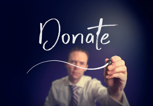 A businessman writing a Donate concept with a white pen on a clear screen.