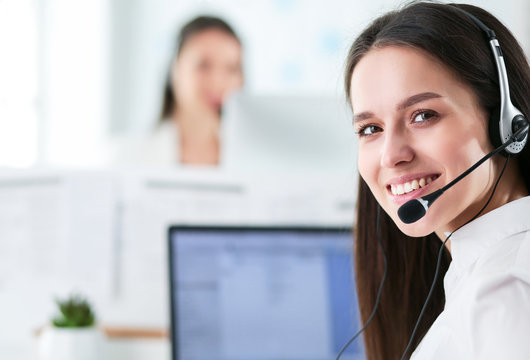 Smiling businesswoman or helpline operator with headset and computer at office