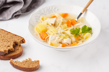Chicken soup with noodles and vegetables in a white plate.