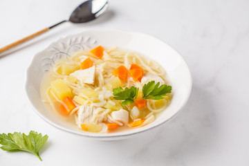 Chicken soup with noodles and vegetables in a white plate.
