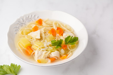Chicken soup with noodles and vegetables in a white plate.