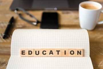 Closeup on notebook over vintage desk background, front focus on wooden blocks with letters making Education text