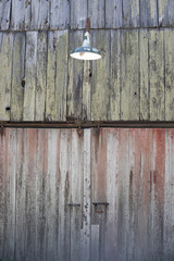 Detail of the side of a weathered barn with an old green light fixture.