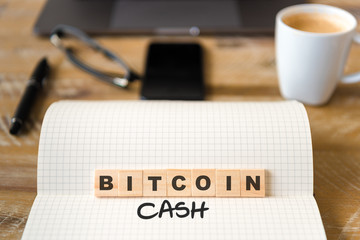 Closeup on notebook over vintage desk background, front focus on wooden blocks with letters making Bitcoin Cash text