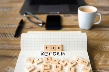 Closeup on notebook over vintage desk background, front focus on wooden blocks with letters making Tax Reform text