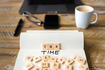 Closeup on notebook over vintage desk background, front focus on wooden blocks with letters making Tax Time text