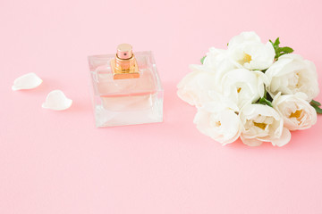 Perfume bottle on pastel pink table. Beautiful, fresh bouquet of white roses. Care about fresh fragrance of woman's body. Mockup for special offers as advertising or other ideas.