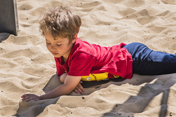 Ein Junge spielt mit Sand, ein Junge im Sandkasten, Ein Junge liegt im Sand