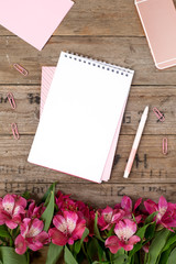 Empty white notepad with pink and white paper with flowers,pink phone and pen on vintage wooden table 