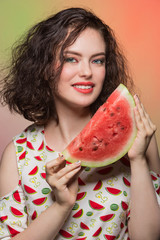 young girl with beautiful make-up is holding a watermelon slice and smiling, emotions and gestures, on a colorful background, summer concept and food